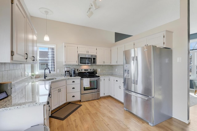 kitchen featuring light stone counters, a sink, decorative backsplash, light wood-style floors, and appliances with stainless steel finishes