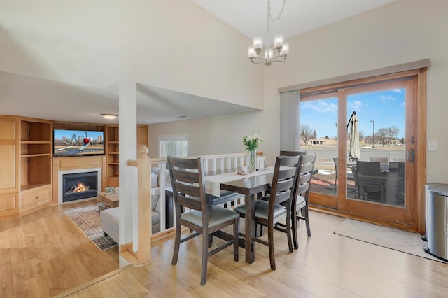 dining space featuring plenty of natural light, light wood-style floors, a warm lit fireplace, and a chandelier