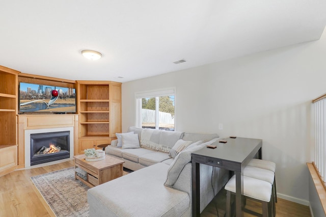 living area featuring a glass covered fireplace, wood finished floors, visible vents, and baseboards