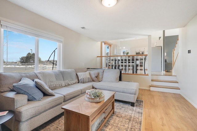 living area featuring stairs, light wood-style floors, visible vents, and baseboards