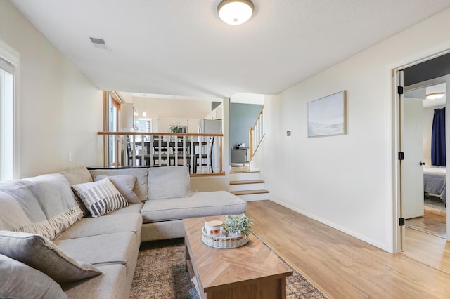 living area featuring light wood-type flooring, visible vents, plenty of natural light, and stairway