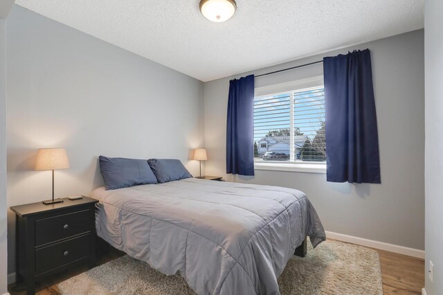 bedroom with wood finished floors, baseboards, and a textured ceiling