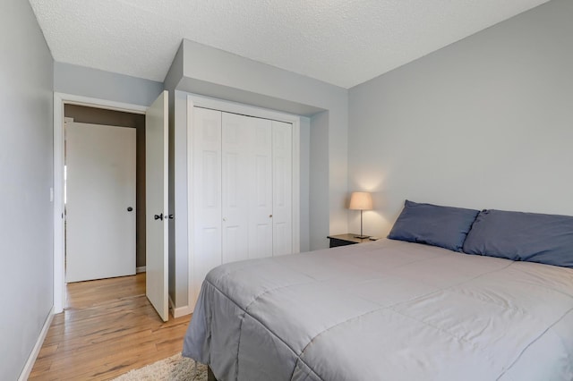 bedroom featuring a closet, baseboards, light wood-style floors, and a textured ceiling