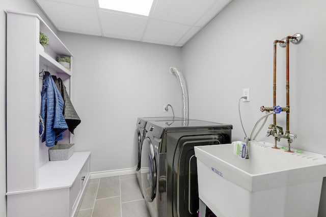 washroom featuring baseboards, washing machine and dryer, laundry area, light tile patterned flooring, and a sink