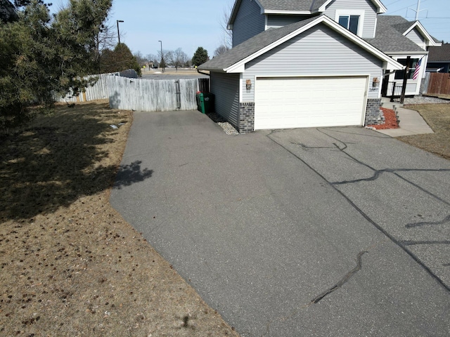 view of side of home with fence, driveway, a shingled roof, a garage, and brick siding