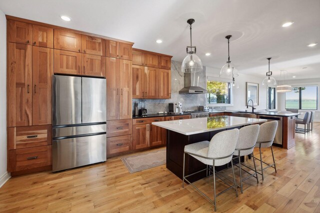 kitchen featuring stainless steel appliances, a peninsula, wall chimney range hood, a center island, and tasteful backsplash