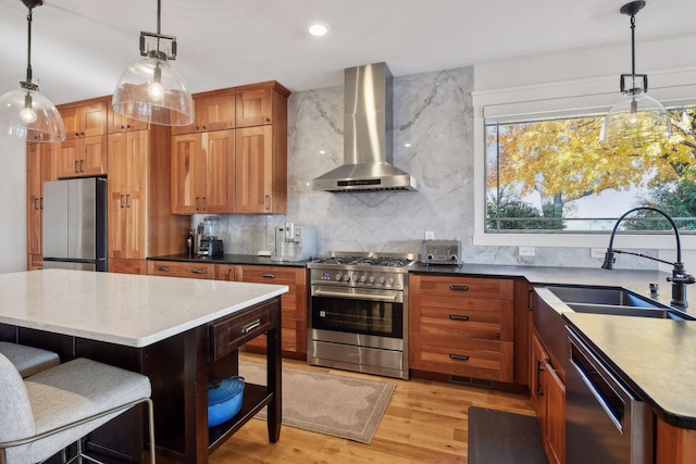 kitchen with a sink, light wood-style floors, appliances with stainless steel finishes, backsplash, and wall chimney exhaust hood