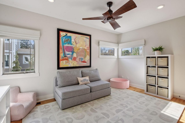 sitting room with baseboards, plenty of natural light, wood finished floors, and recessed lighting