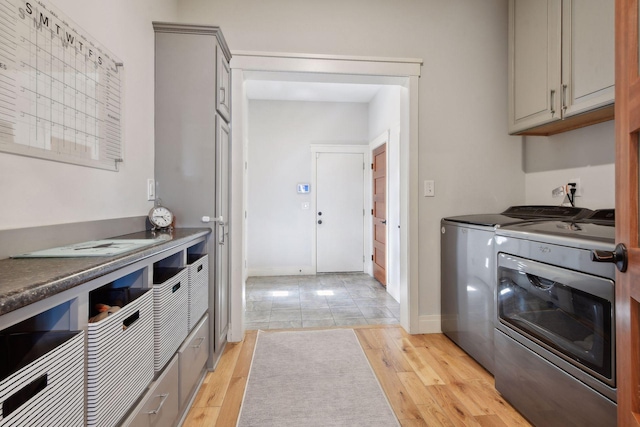 kitchen featuring baseboards, dark countertops, gray cabinetry, light wood-type flooring, and washing machine and dryer