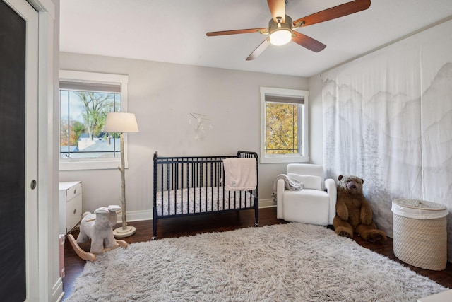 bedroom featuring a nursery area, multiple windows, baseboards, and wood finished floors