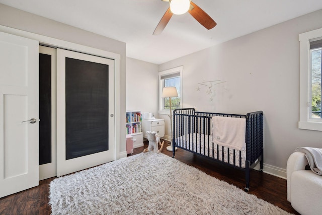 bedroom featuring baseboards, a ceiling fan, wood finished floors, a nursery area, and a closet