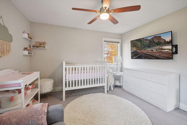 carpeted bedroom featuring a crib, ceiling fan, and baseboards