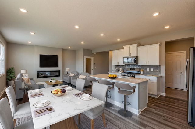 dining area featuring baseboards, dark wood-style flooring, a glass covered fireplace, and recessed lighting