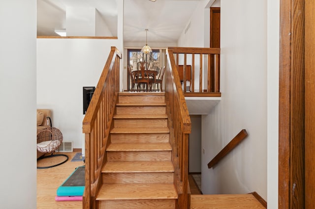 staircase featuring a notable chandelier, wood finished floors, and visible vents