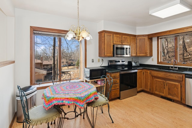 kitchen featuring light wood-type flooring, a sink, dark countertops, stainless steel appliances, and brown cabinetry