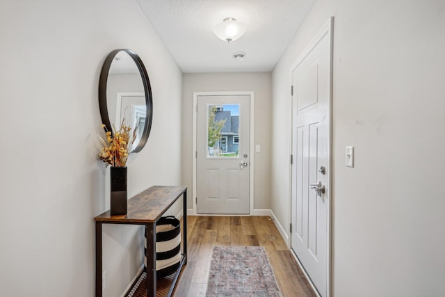 entryway with light wood-type flooring, baseboards, and a textured ceiling