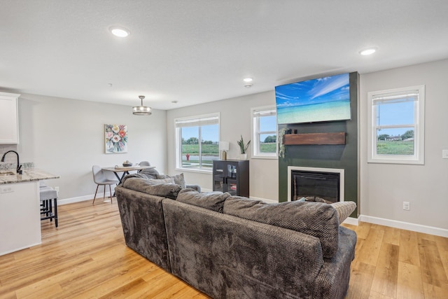 living room featuring light wood-style floors, recessed lighting, a large fireplace, and baseboards