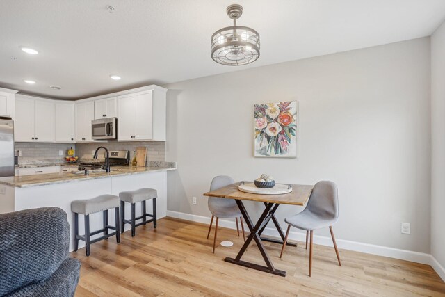 kitchen featuring stainless steel appliances, tasteful backsplash, light wood-style flooring, and white cabinetry