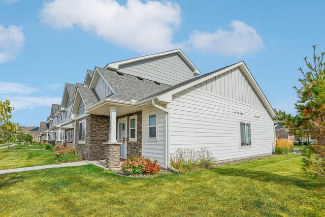 view of side of property featuring board and batten siding, stone siding, a lawn, and a shingled roof