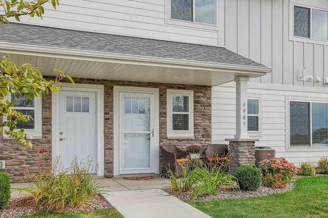 entrance to property featuring stone siding, a shingled roof, board and batten siding, and central air condition unit