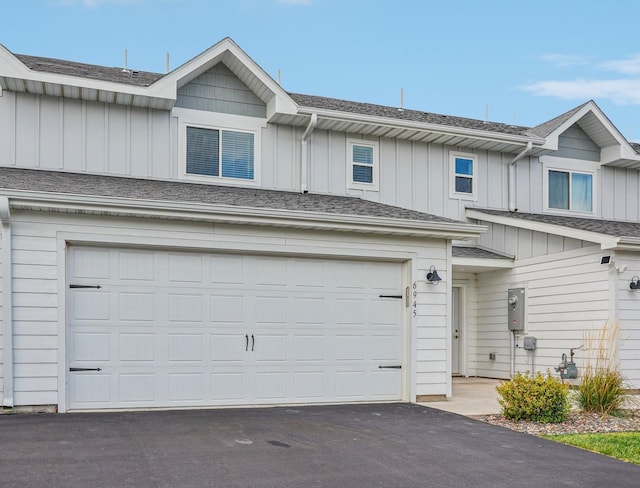 view of property with a garage, driveway, a shingled roof, and board and batten siding