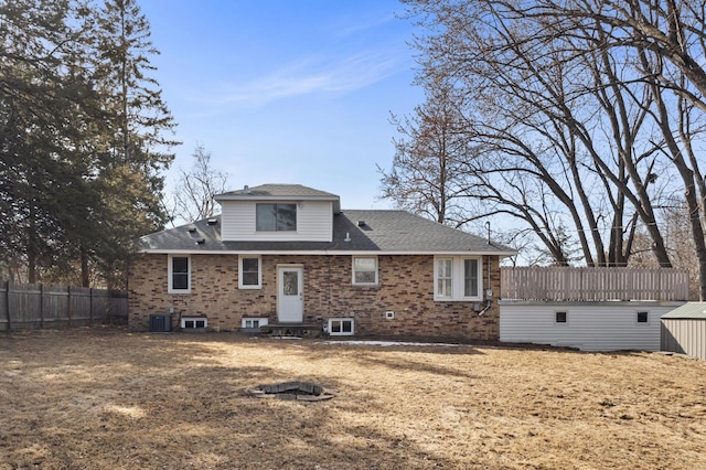 back of property featuring brick siding, central AC unit, a shingled roof, and fence