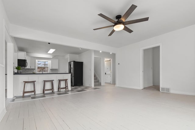 unfurnished living room with visible vents, light wood finished floors, ceiling fan, stairs, and a sink