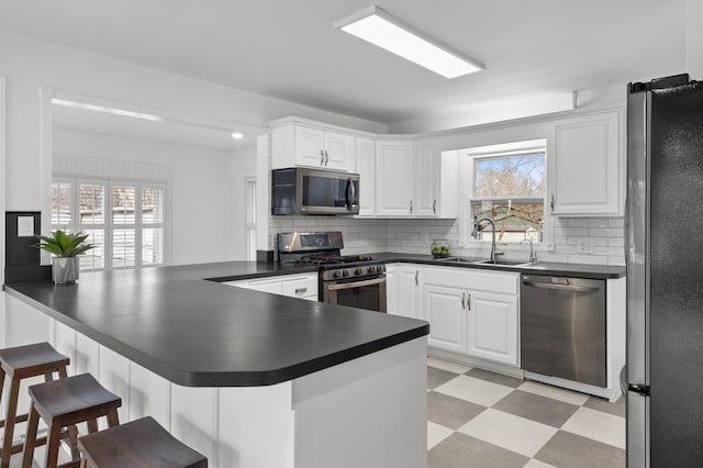 kitchen with a sink, dark countertops, appliances with stainless steel finishes, a breakfast bar area, and light floors