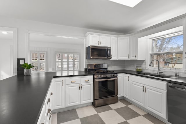 kitchen featuring light floors, a sink, appliances with stainless steel finishes, white cabinetry, and dark countertops