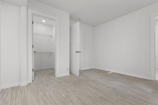 unfurnished bedroom with a walk in closet, baseboards, and light colored carpet