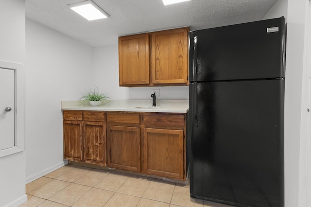 kitchen with a sink, freestanding refrigerator, brown cabinetry, light countertops, and light tile patterned floors