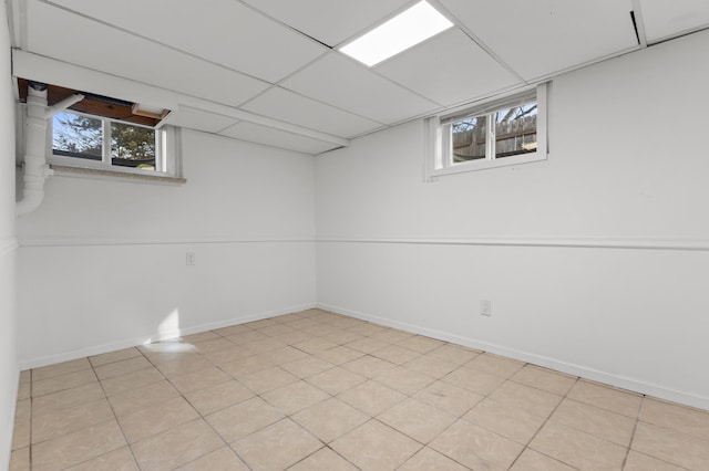 basement with a drop ceiling, a healthy amount of sunlight, and baseboards