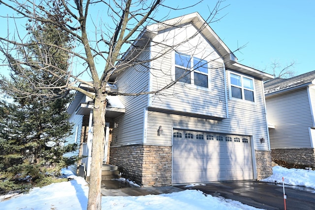 view of snow covered exterior with a garage and stone siding