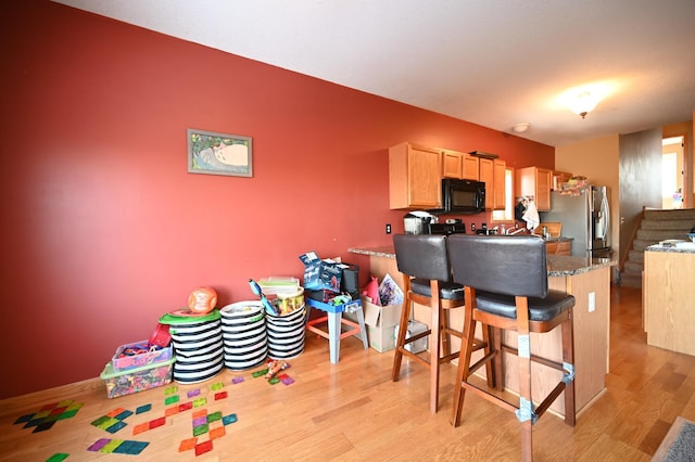 kitchen featuring black microwave, a breakfast bar area, light wood-type flooring, a peninsula, and stainless steel fridge