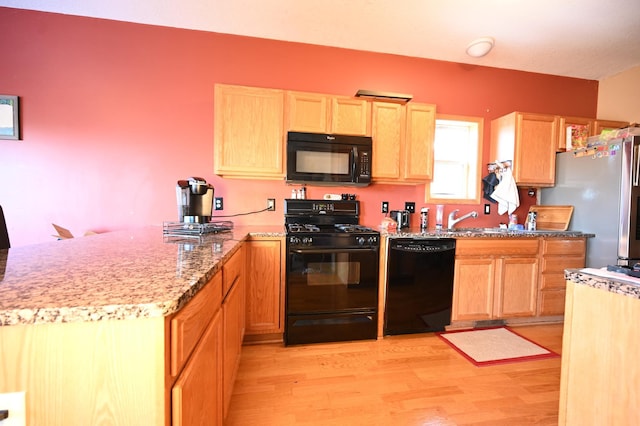 kitchen featuring light brown cabinetry, light wood-type flooring, a peninsula, black appliances, and a sink