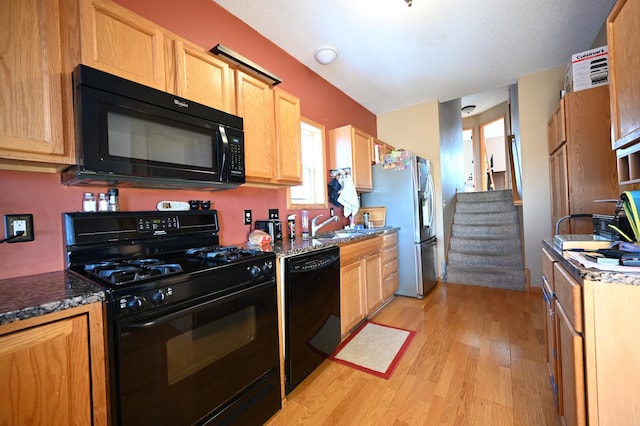 kitchen featuring black appliances, light wood finished floors, and a sink