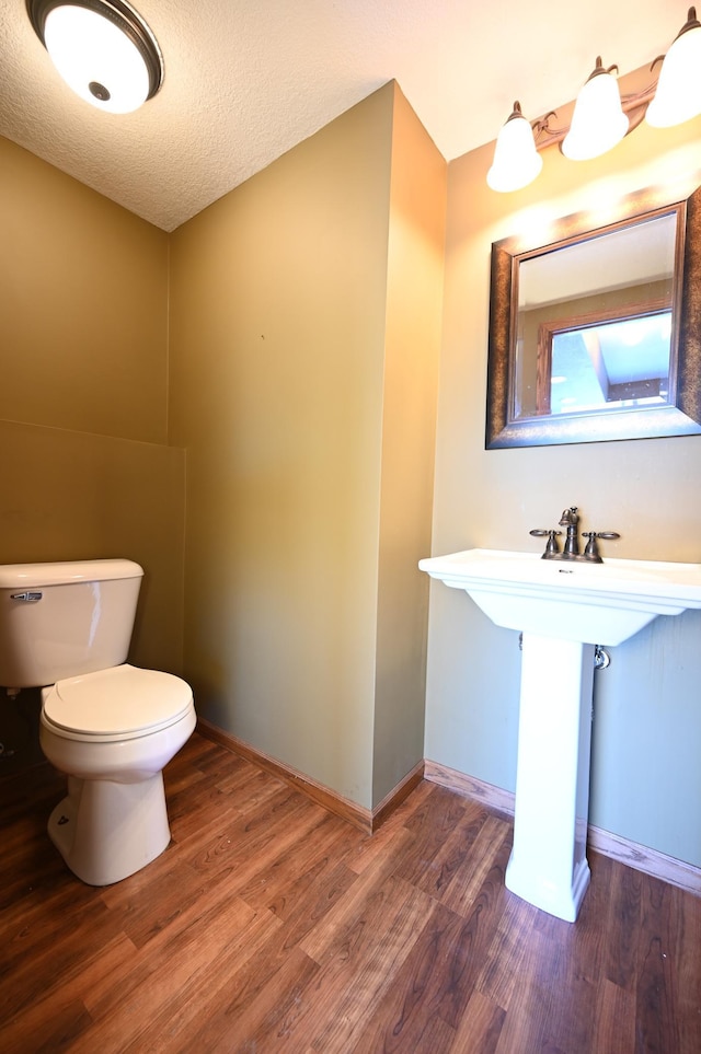 bathroom featuring a textured ceiling, toilet, baseboards, and wood finished floors