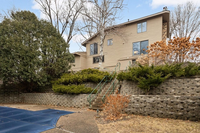 back of house with stairway, a fenced in pool, and a chimney