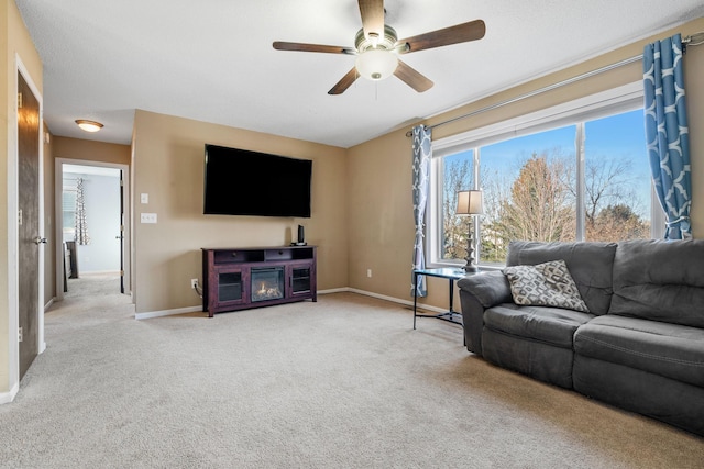 living area featuring a glass covered fireplace, a ceiling fan, baseboards, and carpet floors