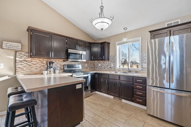 kitchen featuring a peninsula, light wood-style flooring, a sink, stainless steel appliances, and vaulted ceiling