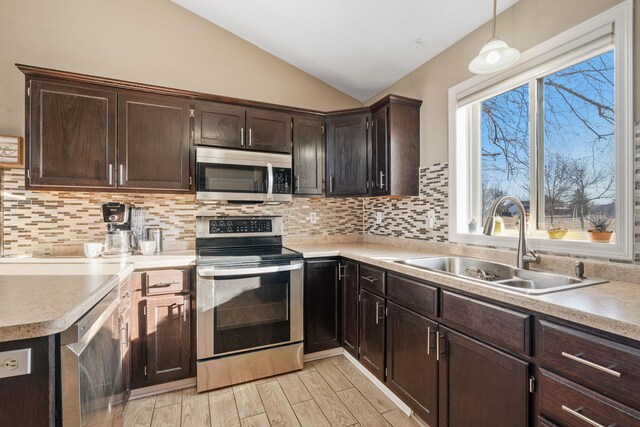 kitchen with light wood finished floors, lofted ceiling, a sink, stainless steel appliances, and backsplash