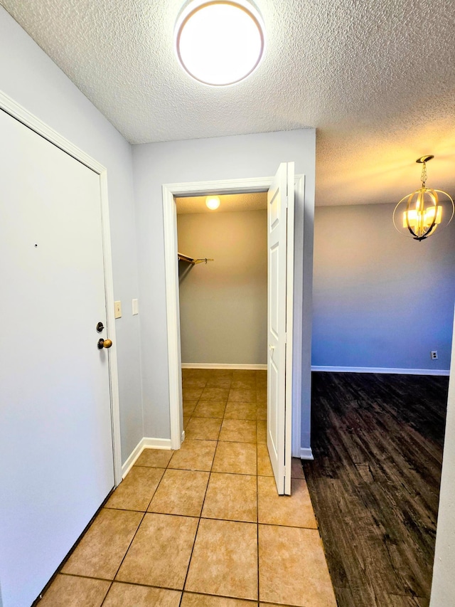 hall with a notable chandelier, a textured ceiling, baseboards, and light tile patterned floors