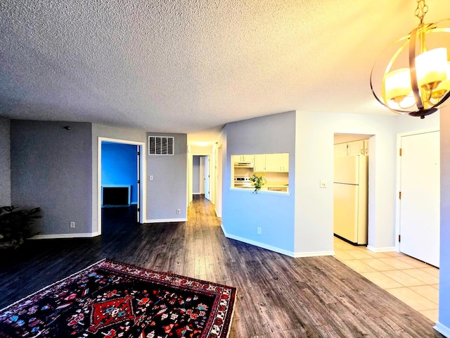 unfurnished living room with baseboards, a textured ceiling, visible vents, and wood finished floors