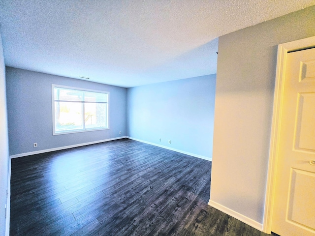 empty room with dark wood-style floors, visible vents, baseboards, and a textured ceiling