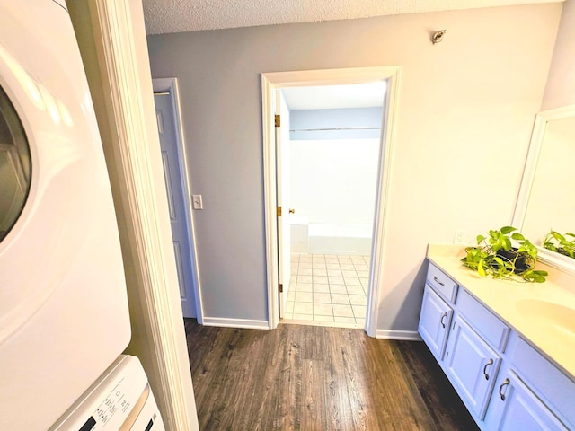 bathroom featuring baseboards, wood finished floors, a textured ceiling, vanity, and stacked washing maching and dryer