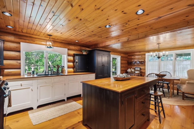 kitchen with wood counters, a sink, light wood-style floors, white cabinetry, and a notable chandelier