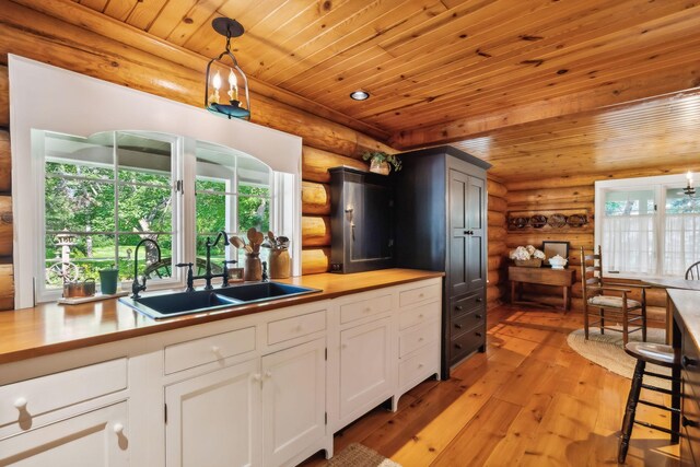 kitchen with wooden ceiling, a sink, light wood-style floors, white cabinets, and pendant lighting