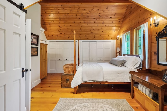 bedroom featuring light wood-type flooring, a barn door, vaulted ceiling, and two closets