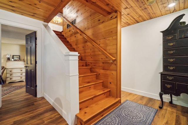 staircase with a notable chandelier, wood finished floors, wood ceiling, and baseboards