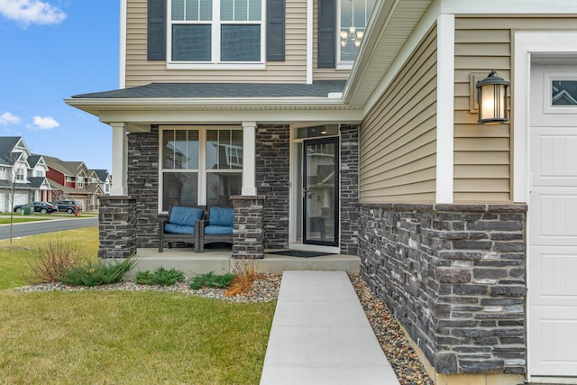 view of exterior entry featuring covered porch, a shingled roof, stone siding, and a lawn